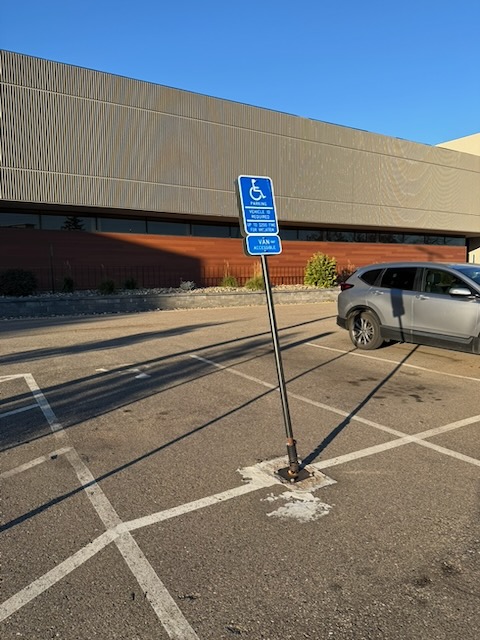 車いすユーザーのための駐車スペースを意味する標柱の画像。斜めに傾いている。よく見ると根本部分がバネ構造になっている。
